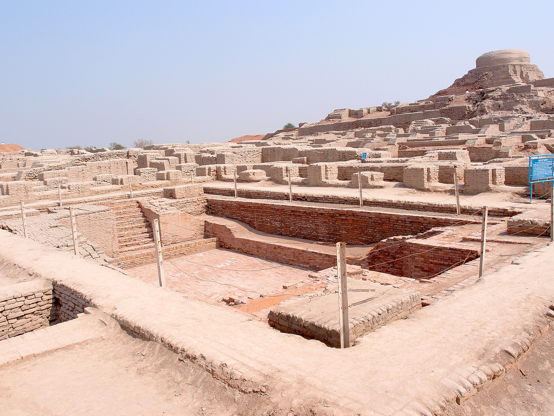 Mudbrick ruins of Mohenjo-daro with a large rectangular sunken bath and a mound behind